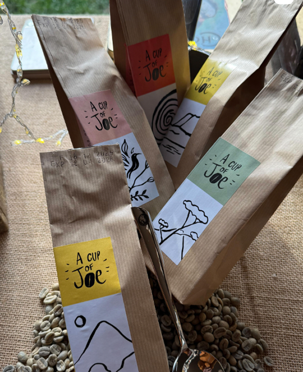 Des paquets de café A Cup of Joe posés sur une toile de jute, avec des grains verts