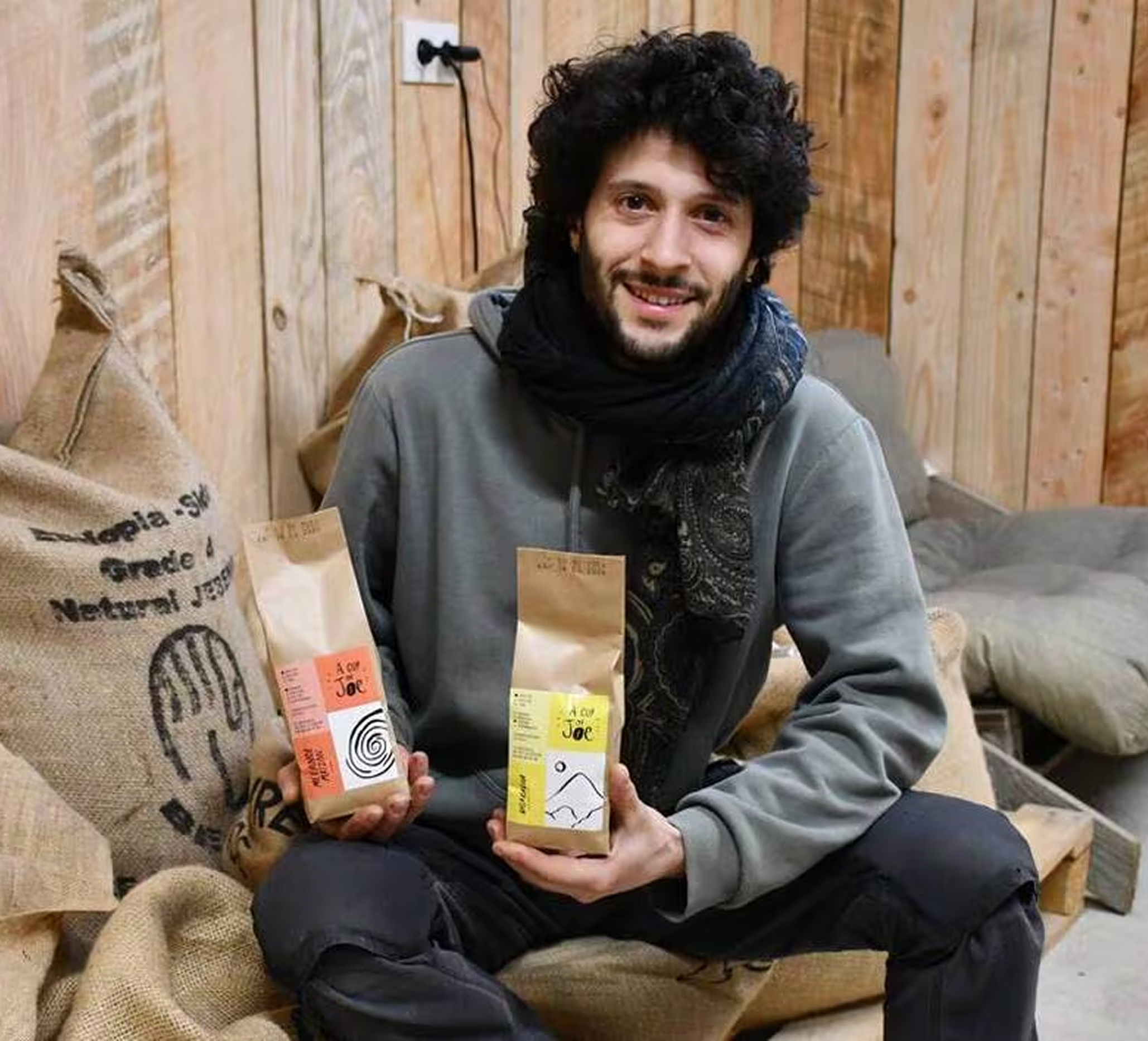 Jozef, le torréfacteur, assis avec deux paquets de café dans les mains